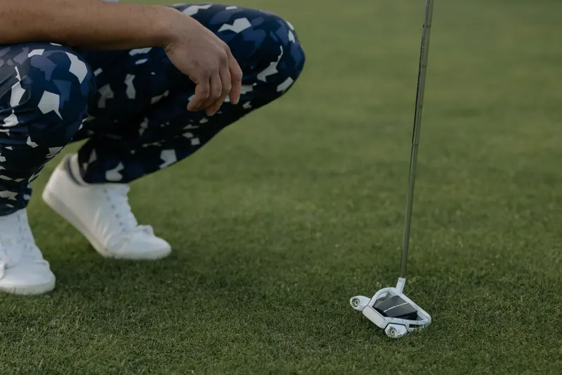 Golfer in patterned pants squatting with putter on grass ready to strike