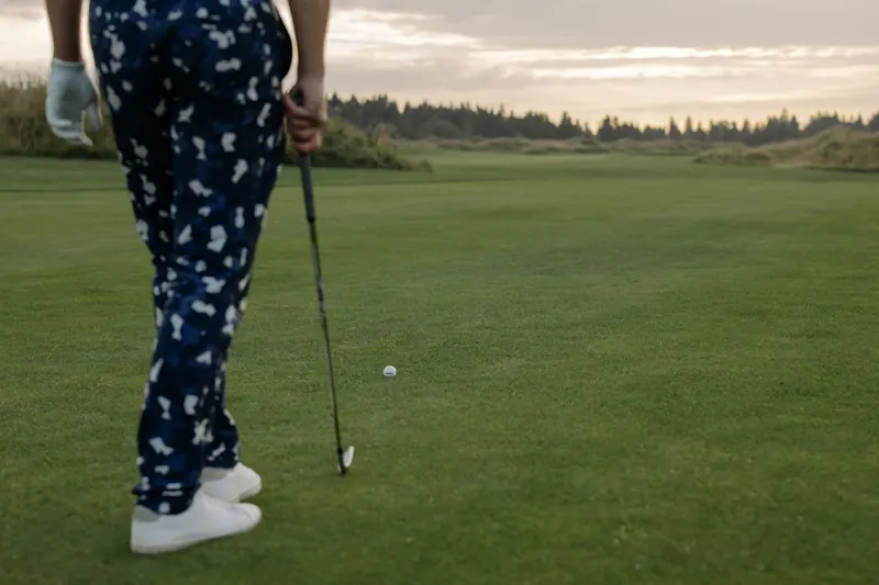 Golfer standing on a putting green, ready to putt at sunset, wearing patterned pants