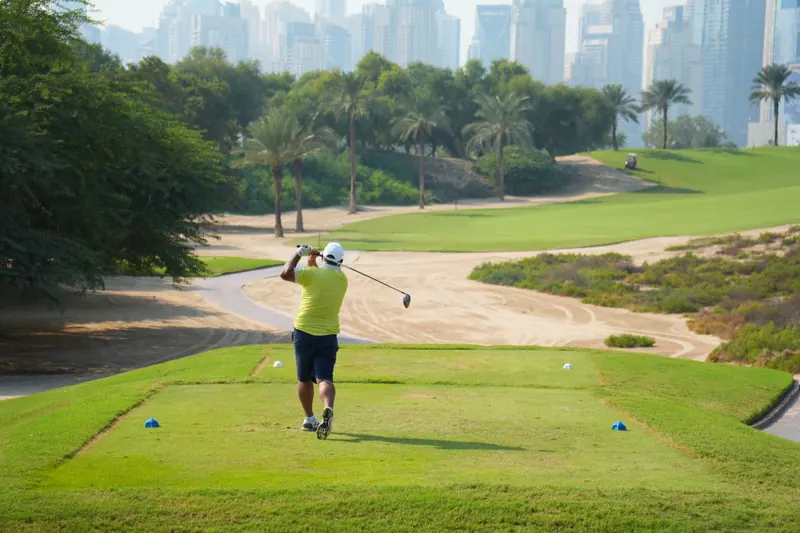 A golfer teeing off on a sunny day with the iconic Dubai skyline in the backdrop