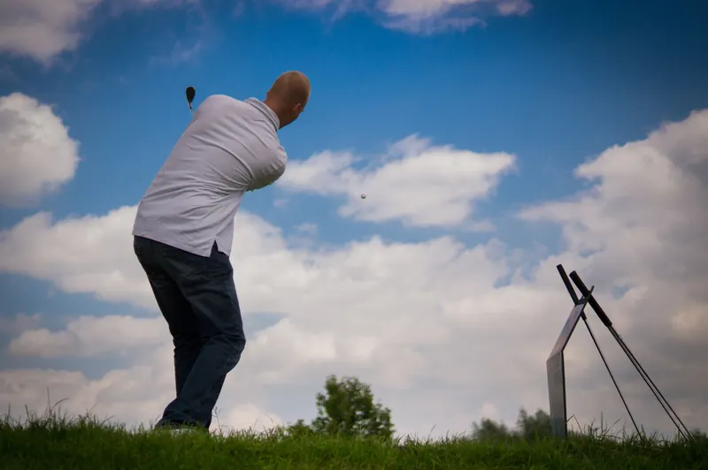 A golfer in mid-swing on a sunny day with a vibrant blue sky