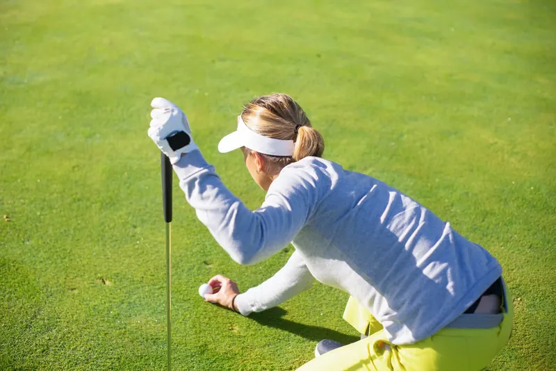 Female golfer in a gray sweater prepares to putt on a bright day outdoors
