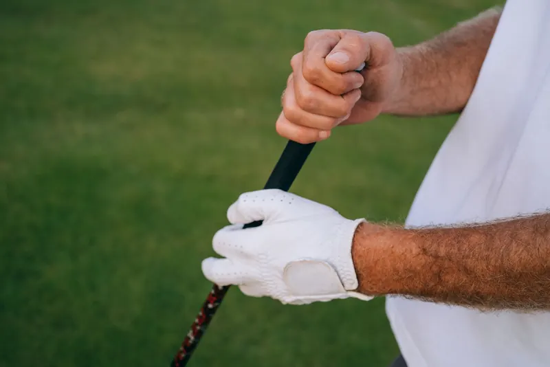 Close-up of a golfer's hands gripping a club, wearing white gloves on a green course
