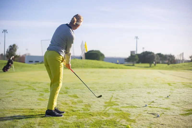 A woman golfer practicing on a sunny course, using a driver, on lush green grass