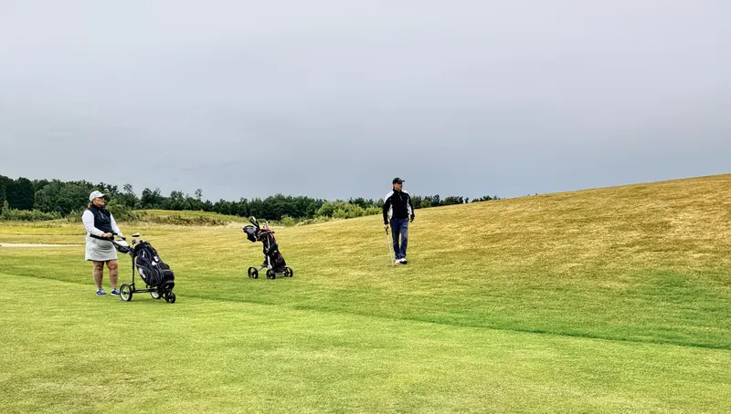 Two golfers on a lush green course in Skåne, Sweden, enjoying a leisurely game under a cloudy sky