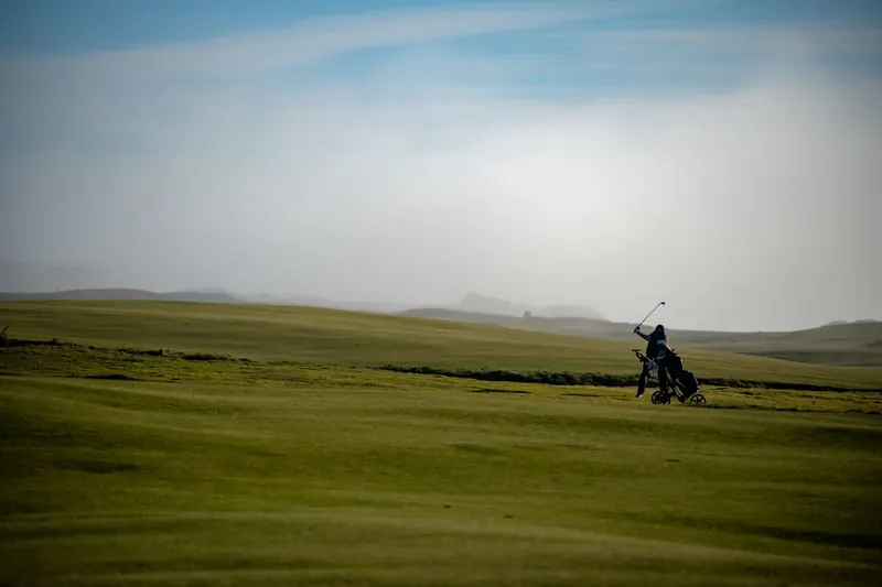 A golfer swings on a vast, misty course under a clear sky, illustrating serene sportsmanship